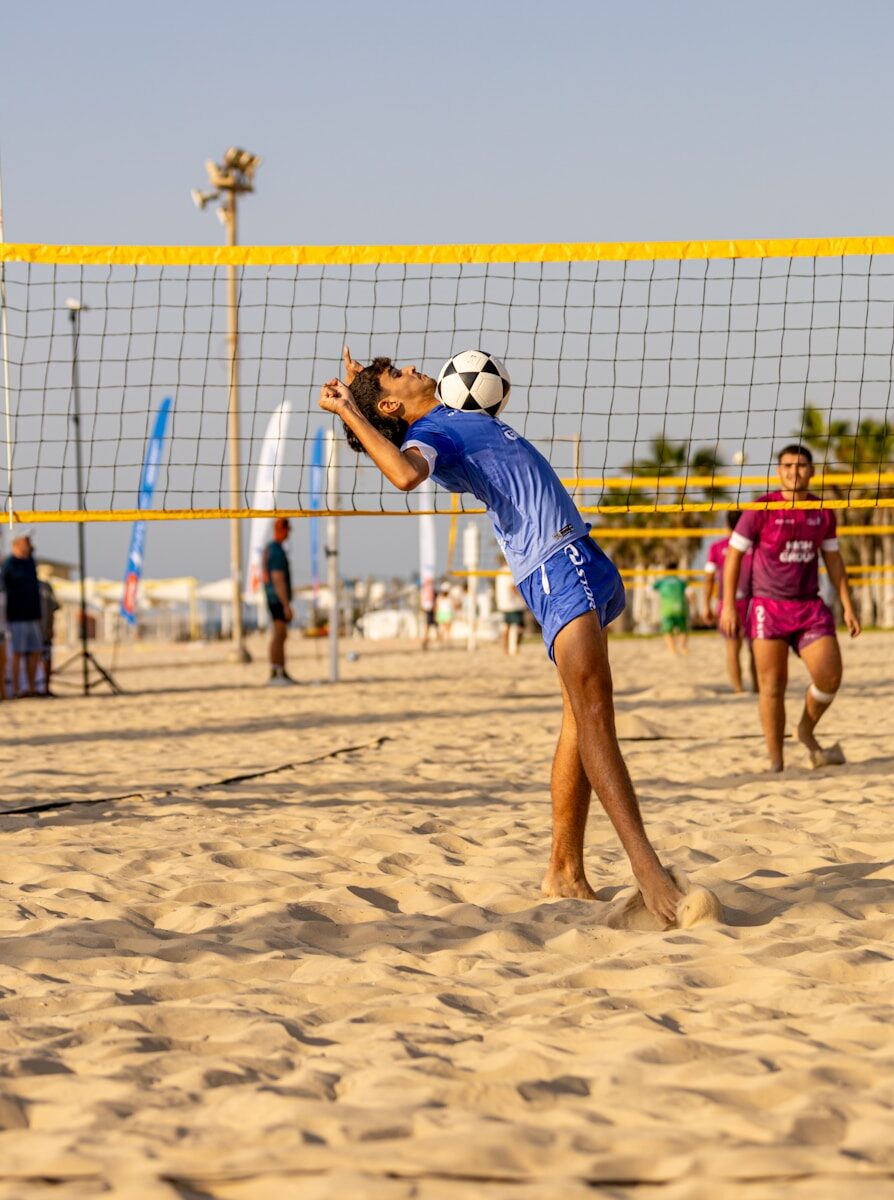 Young man balancing soccer ball on his head on beach.